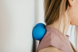 Close-up of woman using blue massage balls for neck relief against a wall.