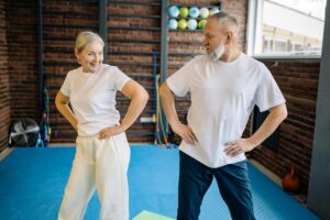 Elderly couple in white shirts having fun exercising indoors for fitness and wellness.