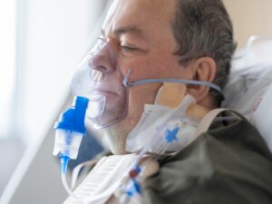 A senior adult patient using an oxygen mask in a hospital setting for medical care.