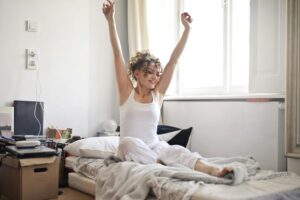A happy woman stretches on her bed in a bright, cozy bedroom, embracing a new day.