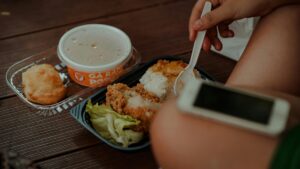 A hand holding a spoon near a meal of fried chicken, rice, and soup.