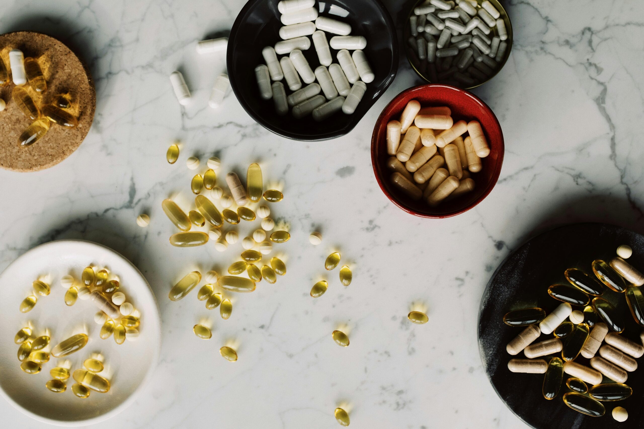 Assorted capsules and pills on a marble surface, illustrating healthcare and medication themes.