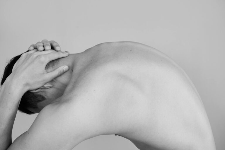 Black and white studio shoot capturing a man's shirtless bent posture highlighting the male torso.