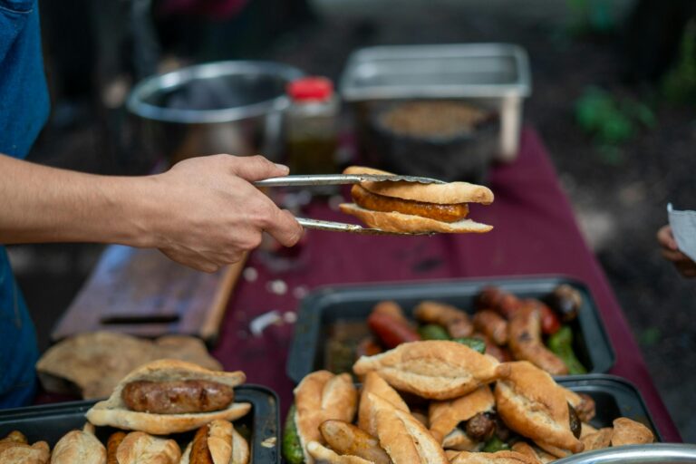 Street vendor grilling sausage sandwiches on a sunny day. Vibrant outdoor food scene with diverse offerings.
