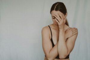 Young slender female with closed eyes covering breast and face on grey background