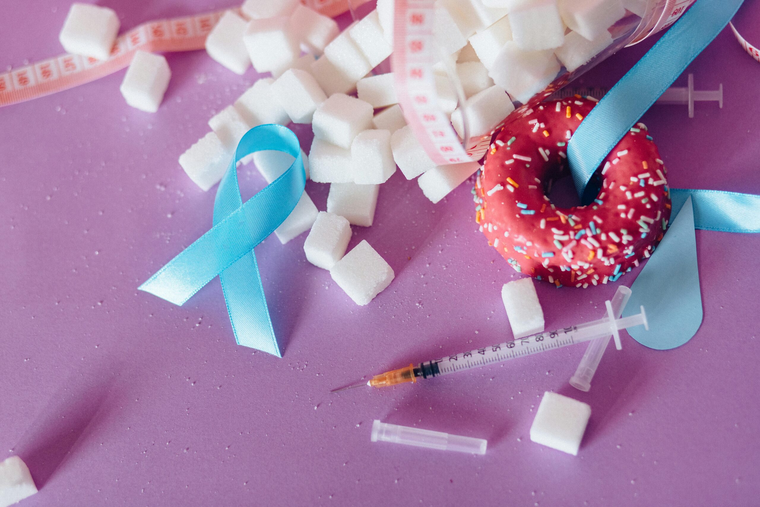 Creative composition highlighting diabetes awareness with donut, syringe, and sugar cubes on purple background.